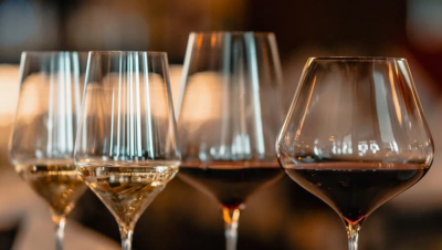 Nahaufnahme von vier Weingläsern auf einem Tisch, gefüllt mit Weiß- und Rotwein, vor einem warmen, unscharfen Hintergrund.