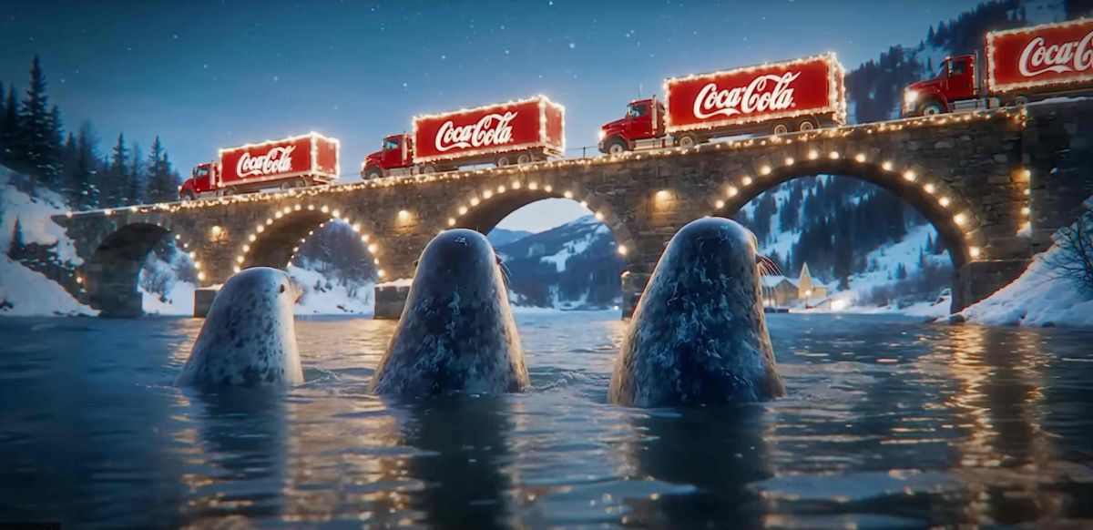 Mehrere rot beleuchtete Lastwagen fahren bei Schneefall durch eine winterlich geschmückte Straße mit historischen Häusern und Weihnachtsbeleuchtung.