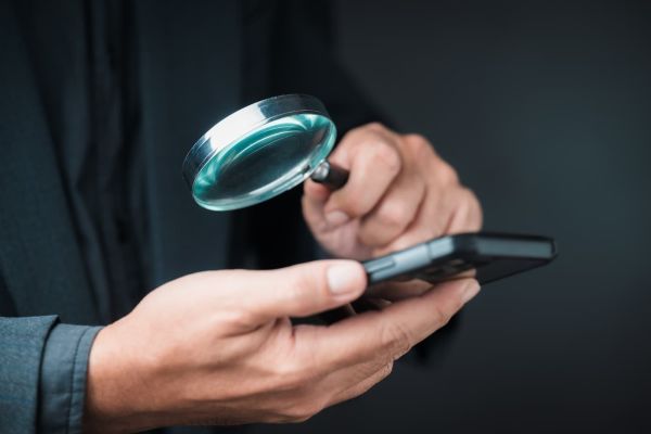 Eine Lupe über einem Smartphone als Symbolbild für die KI Konsum Studie