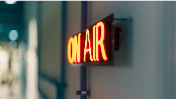 Leuchtendes rotes „On Air“-Schild an einer Wand, unscharfer Hintergrund mit Lichtreflexen.