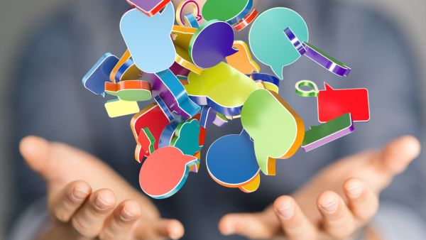 Zwei geöffnete Hände halten scheinbar eine bunte Wolke aus Sprechblasen und Symbolen in der Luft. Das Bild visualisiert Kommunikation, Ideenvielfalt, Austausch und digitale Vernetzung im Raum online!